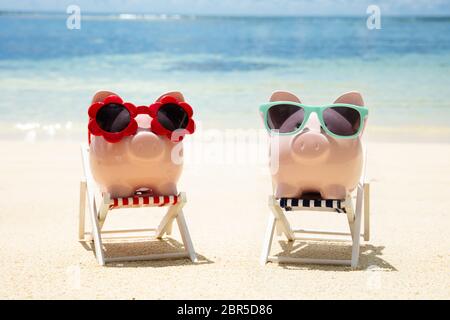 Close-up of Pink Piggybanks avec différent type de lunettes de soleil sur une chaise longue à Beach Banque D'Images