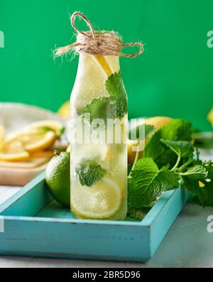 Boisson froide avec les citrons, les feuilles de menthe, la chaux dans une bouteille de verre, près de les ingrédients pour faire de la limonade , fond vert Banque D'Images
