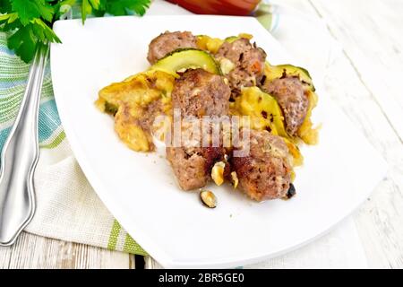 Des boulettes de viande cuite au four avec les courgettes, le fromage et les noix dans un plat sur une serviette, le persil et la fourche sur un fond de bois Banque D'Images