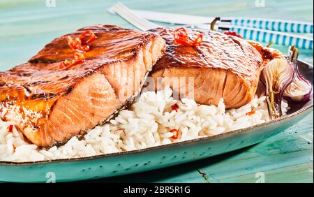 Grillés gourmet ou cuit au four avec des darnes de saumon épicé de piment rouge sur un lit de riz servi avec des oignons grillés dans une vue en gros plan d'une publicité menu Banque D'Images