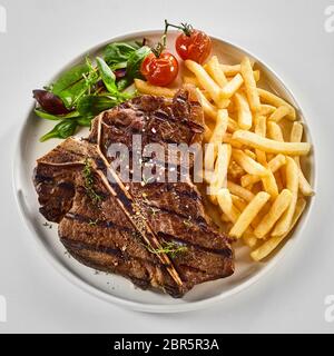 Grillé au barbecue savoureux ou T-bone steak avec des croustilles de pommes de terre frites, salade verte et tomates rôties au vu de dessus en format carré blanc Banque D'Images