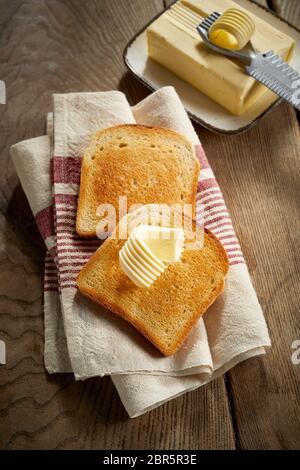 Deux tranches de pain blanc doré croustillant toast avec une boucle de beurre frais de la ferme rustique sur un tissu à rayures sur une table vue high angle Banque D'Images