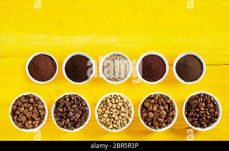 Assortiment de grains de café torréfié et de matières premières avec des motifs dans des bols en deux lignes sur un fond de bois jaune with copy space Banque D'Images