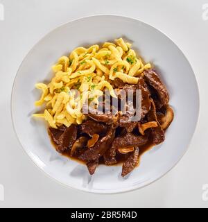 Assiette de ragoût de Suisse avec des lamelles de viande et de champignons dans une sauce riche servi avec des nouilles isolé sur un fond blanc dans une vue du haut vers le bas dans la région de squar Banque D'Images