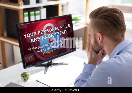 Inquiets Businessman Looking At Computer avec Ransomware mots à l'écran sur le lieu de travail Banque D'Images
