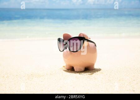 Pink Piggybank portant des lunettes noires sur le sable à la plage Banque D'Images