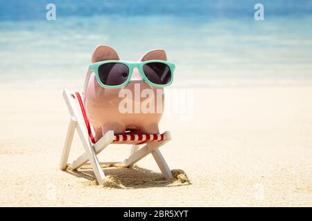 Close-up of Pink Piggybank avec lunettes Turquoise sur une chaise Miniature sur Sand At Beach Banque D'Images