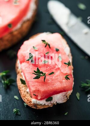 Toasts avec du fromage à pâte molle, de la pastèque et thym frais.salé sucré,fromage pastèque et épicé sur croquant de thym pain grillé tranches. Idée et recette pour Banque D'Images