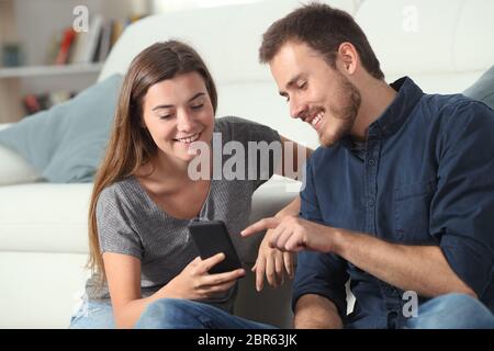 Heureux couple checking smart phone apps assis sur un canapé dans la salle de séjour à la maison Banque D'Images