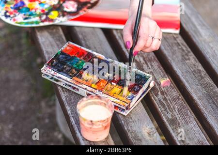 Fille dessine une photo tout en étant assis sur un banc dans un parc. Le peintre mélange les peintures pour peindre une image Banque D'Images