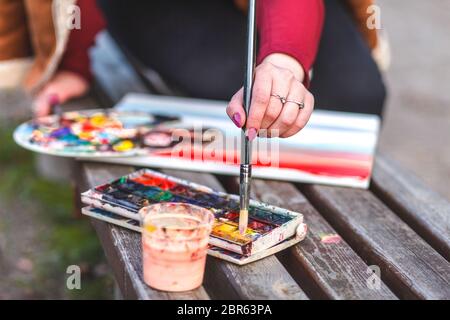 Fille dessine une photo tout en étant assis sur un banc dans un parc. Le peintre mélange les peintures pour peindre une image Banque D'Images