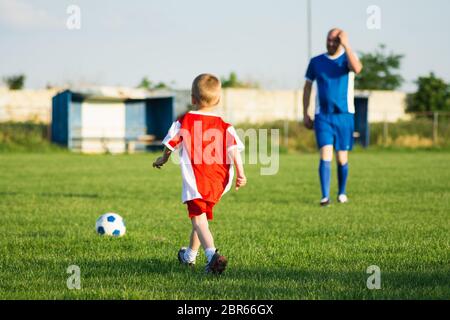 Petit garçon de football en rouge et entraîneur en robe de football bleu jouent au football sur le terrain, le concept de formation de football pour enfants. Banque D'Images