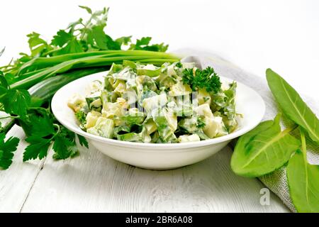 Salade de concombre, oseille, pommes de terre bouillies, les oeufs et les herbes, habillé avec de la mayonnaise dans une assiette blanche, le persil, les oignons verts et la serviette contre l'arrière Banque D'Images