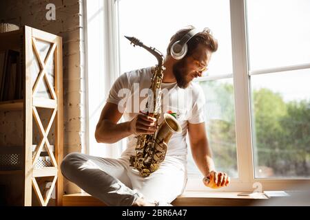 Musicien caucasien jouant du saxophone pendant un concert en ligne à la maison isolé et mis en quarantaine. Utilisation de l'appareil photo, de l'ordinateur portable, de la diffusion en continu et de l'enregistrement de Concept d'art, de soutien, de musique, de passe-temps, d'éducation. Banque D'Images