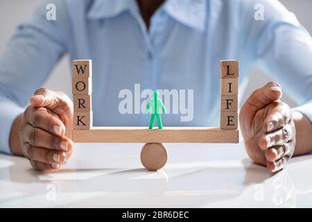 La figure humaine se tenant entre le travail et la vie des blocs de bois sur Seesaw protégée par Businesswoman Banque D'Images