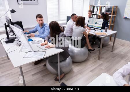 Groupe de Multi-ethnic Woman Sitting on Fitness Ball avoir discuter tout en travaillant à l'Office de Tourisme Banque D'Images