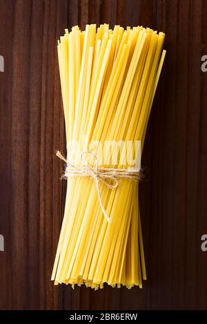 Long ruban plat brut appelé pâtes Fettuccini ficelés, photographié dans le ciel en bois Banque D'Images