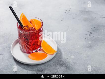 Cocktail Negroni en verre cristal dans une plaque en céramique blanche avec tranche d'orange et paille noire sur fond de table lumineuse. Vue de dessus Banque D'Images