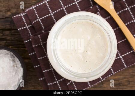 Des bubbly levain fermenté, un mélange d'eau et de farine à utiliser comme ferment pour la cuisson du pain, dans un bocal en verre avec de la farine et en bois Banque D'Images