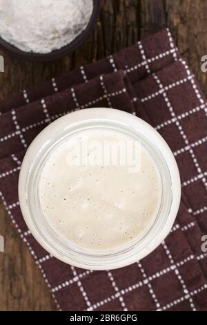 Des bubbly levain fermenté, un mélange d'eau et de farine à utiliser comme ferment pour la cuisson du pain, dans un bocal en verre avec de la farine sur le côté Banque D'Images