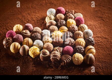 Mise en page en forme de coeur de bonbons au chocolat fantaisie divers assis sur la surface de la poudre de cacao brun viewed in close-up Banque D'Images