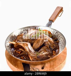 Quartiers de lapin sauvage rôti assaisonné d'orange, les herbes, l'ail dans une casserole en cuivre avec de la sauce sur une carte ronde isolated on white Banque D'Images