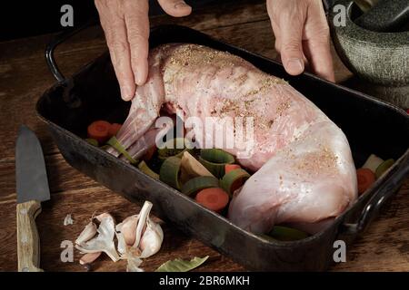 Les mains d'un chef cuisinier de préparer un rôti de chevreuil frottant une spice rub sur le cadavre d'un lapin sauvage dans une rôtissoire avec les poireaux et les carottes Banque D'Images