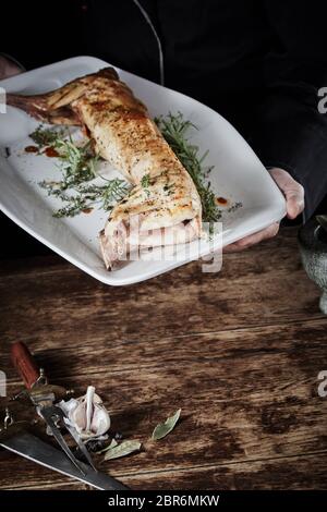 Chevreuil rôti de lapin sauvage sur une grande assiette blanche sur une table rustique avec copie au premier plan l'espace avec l'ail frais et des herbes dans le coin Banque D'Images