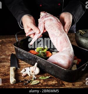 Chef de l'affichage d'une carcasse de lapin sauvage non cuit frais comme il le prépare pour la cuisson à la poêle avec les poireaux, les carottes, l'ail, les herbes et épices Banque D'Images