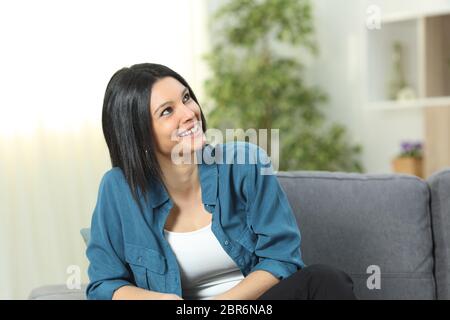 Heureux pensive woman looks ci-dessus assis sur un canapé dans la salle de séjour à la maison Banque D'Images