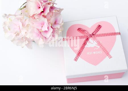 Hortensia rose en forme de boule dans un vase en verre rond avec boîte pour coeur avec inscription meilleurs voeux pour une carte de voeux sur fond blanc Banque D'Images