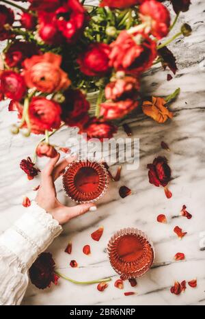 Lit de femme à la main, verre de vin rose profond et bouquet de fleurs de ranunculus rouges sur fond de table en marbre blanc, vue du dessus. Vin de rose Banque D'Images