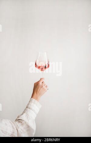 Les femmes sont main dans une chemise blanche tenant un verre de vin rose sur fond de mur blanc. Boutique de vins, dégustation de vins, bar, concept de carte des vins Banque D'Images