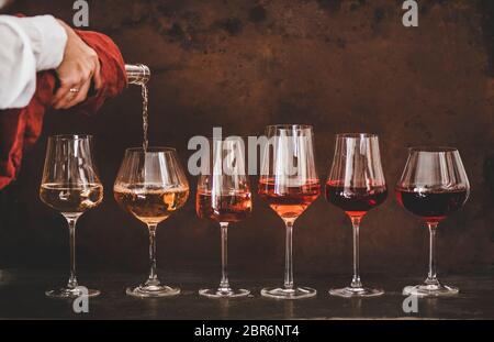 Nuances de vin rose dans verres à pied placés dans la ligne de la lumière à la couleur sombre et les femmes versant main du vin de la bouteille au verre, rouillé dorsté brun backgro Banque D'Images