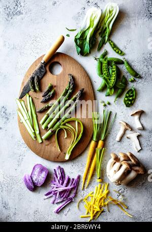 Asperges en tranches sur une planche à découper en bois avec une sélection de légumes frais colorés. Banque D'Images