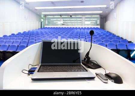 Ordinateur portable et micro sur la tribune dans la salle vide avec des chaises en velours bleu. Banque D'Images