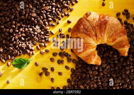 Feuilletée fraîche croissant sur les grains de café torréfié de conceptuel un petit-déjeuner sur un fond jaune colorés disposés en une ligne diagonale Banque D'Images