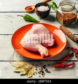 Cuisse de poulet quart sur plaque orange plus de surface en bois avec différentes épices Banque D'Images