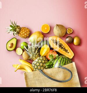 Mise à plat de la vie encore sur un fond rouge est diplômé d'un assortiment de fruits tropicaux frais déborde d'un sac d'épicerie réutilisable dans un concept d'une somme Banque D'Images