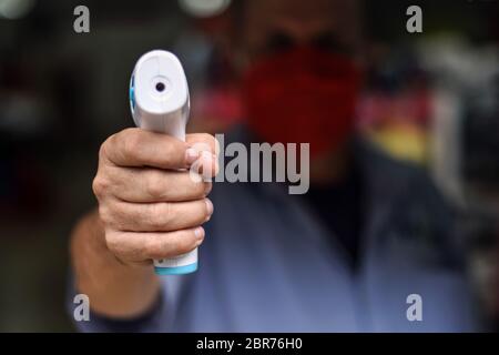 Ouvrier de magasin pointant thermomètre pistolet avant d'entrer dans le local, Colombie Banque D'Images