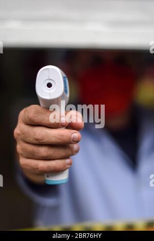 Ouvrier de magasin pointant thermomètre pistolet avant d'entrer dans le local, Colombie Banque D'Images