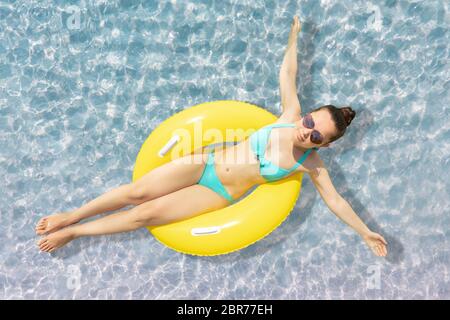 Portrait d'une femme flottant sur le flotteur jaune dans l'eau peu profonde à la plage Banque D'Images
