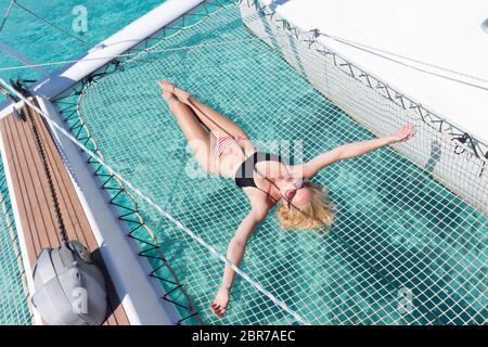 Womanin bronzage bikini et reposant sur un été glaciaire voile croisière, couché dans un hamac de catamaran de luxe près de la plage de sable blanc de Spargi j Banque D'Images