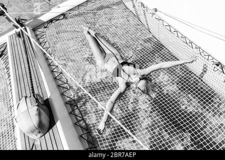 Womanin bronzage bikini et reposant sur un été glaciaire voile croisière, couché dans un hamac de catamaran de luxe bateau. Image en noir et blanc. Banque D'Images