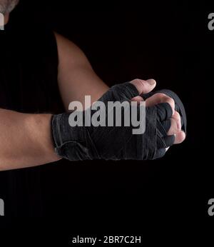 Deux mains d'homme enveloppé dans un bandage textile sports noir, fond noir, athlète avant la lutte Banque D'Images