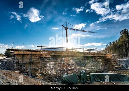 Photo en gros plan du nouveau site de construction de pont avec construction à temps pour le remplir de béton. Tour de grue jaune, contre le soleil, ciel profond Banque D'Images