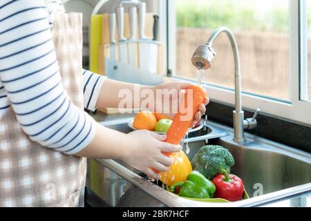 Femme asiatique en bonne santé laver une carotte et d'autres légumes au-dessus de l'évier de cuisine et nettoyer un fruit / légume avec de l'eau pour éliminer les chances de c Banque D'Images