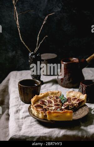 Morceaux de maison pâtisserie de tarte au caramel de pacane américain classique sur plaque de céramique, tasse de café, de la cève, verseuse de crème sur linge de table gris. Banque D'Images