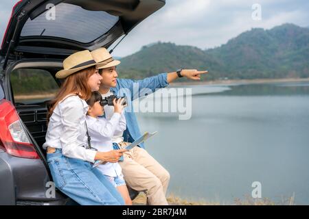 Portrait de la famille asiatique assis en voiture avec le père pointant vers la vue et la mère tenant des cartes avec la fille regardant beau paysage à travers binocul Banque D'Images