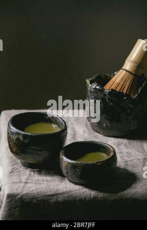 Thé vert matcha japonais dans deux tasses sabi wabi, fouet en bambou sur toile de table grise. Banque D'Images